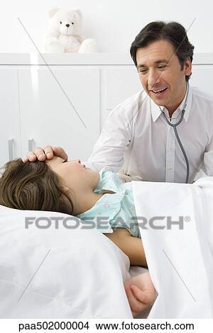 Picture - Girl lying on examination table, doctor touching her forehead. Fotosearch