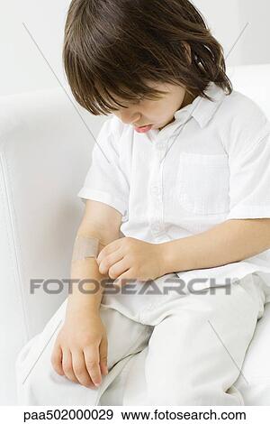 Little boy picking at adhesive bandage on his arm, head down View Large Photo Image Stock Photo - Little boy picking at adhesive bandage on his arm, head down. Fotosearch