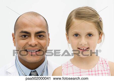 Stock Image - Male doctor beside girl, both smiling at camera, portrait. Fotosearch