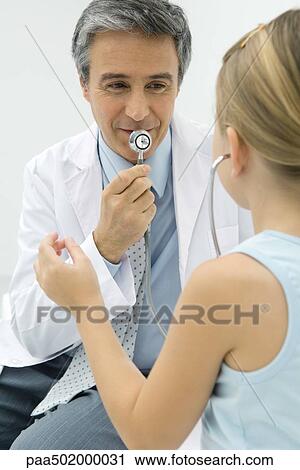 Stock Image - Pediatrician talking into stethoscope, girl listening. Fotosearch