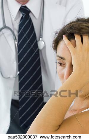 Stock Photo - Woman holding head, looking away, doctor in background. Fotosearch