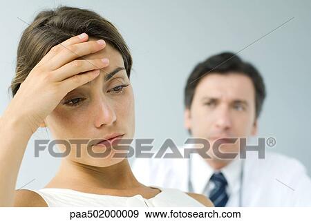Woman holding head, looking down, doctor in background View Large Photo Image Stock Photo - Woman holding head, looking down, doctor in background. Fotosearch