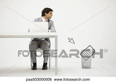 Businessman sitting at desk, looking at computer cursor pointing to document in trash can View Large Photo Image Stock Photograph - Businessman sitting at desk, looking at computer cursor pointing to document in trash can. Fotosearch