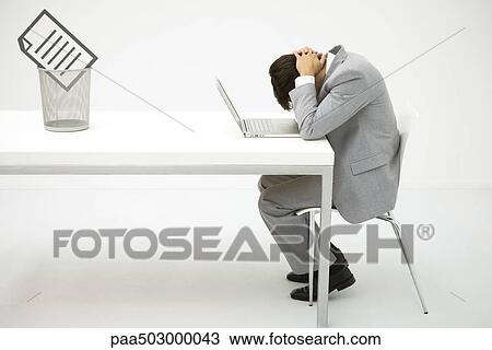 Businessman sitting at desk with head down, document in trash can nearby View Large Photo Image Stock Image - Businessman sitting at desk with head down, document in trash can nearby. Fotosearch
