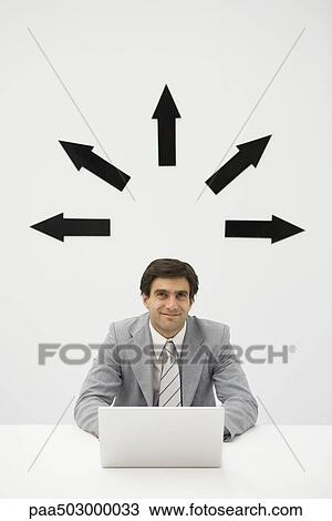 Businessman sitting with laptop, smiling, arrows pointing several directions above his head View Large Photo Image Stock Image - Businessman sitting with laptop, smiling, arrows pointing several directions above his head. Fotosearch