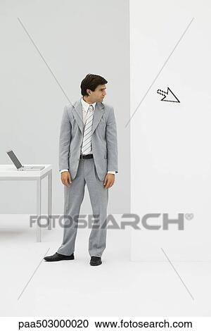Businessman standing in office, looking at computer cursor pointing away View Large Photo Image Stock Image - Businessman standing in office, looking at computer cursor pointing away. Fotosearch