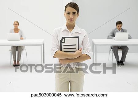Businesswoman holding document, looking at camera, colleagues working in background View Large Photo Image Stock Photography - Businesswoman holding document, looking at camera, colleagues working in background. Fotosearch