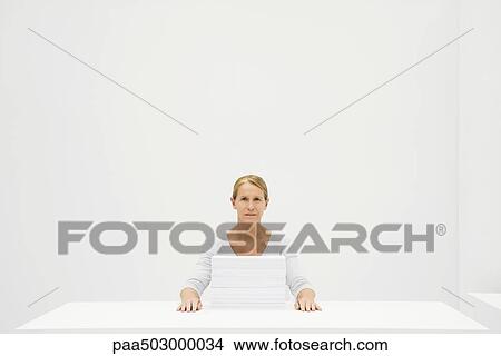 Female office worker sitting behind stack of paper, looking at camera View Large Photo Image Picture - Female office worker sitting behind stack of paper, looking at camera. Fotosearch