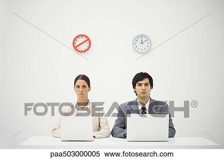 Office workers sitting below clocks, using laptops, warning sign over one clock View Large Photo Image Stock Photography - Office workers sitting below clocks, using laptops, warning sign over one clock. Fotosearch