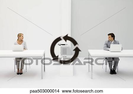 Picture - Office workers sitting with laptops, looking at each other, printer and recycling symbol between them. Fotosearch