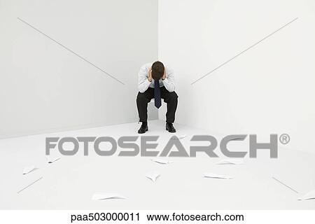 Stock Image - Professional man sitting in corner with head down, paper airplanes littering the floor. Fotosearch