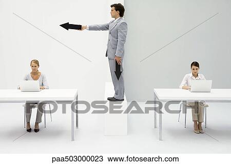 Professional women working in office, man standing between them, pointing arrow View Large Photo Image Stock Image - Professional women working in office, man standing between them, pointing arrow. Fotosearch