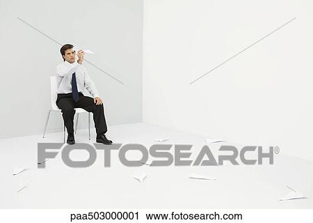 Stock Image - Young professional man sitting in corner, throwing paper airplanes. Fotosearch