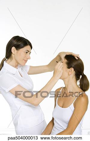 Stock Image - Beautician carefully plucking a woman's eyebrows, smiling. Fotosearch