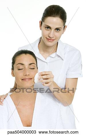 Stock Image - Beautician removing make-up from a woman who has her eyes closed. Fotosearch