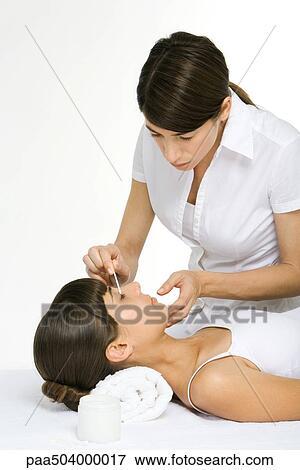 Stock Photo - Beautician rubbing cotton swab over woman's eyelid. Fotosearch