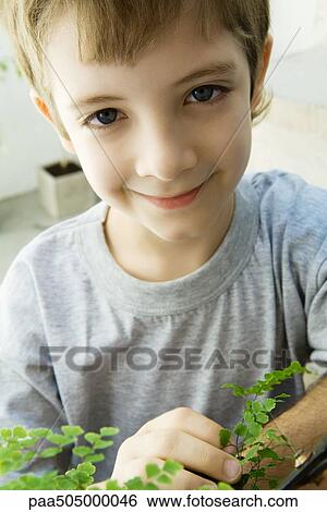 Stock Photograph - Boy touching plant, smiling at camera, close-up. Fotosearch