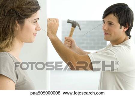 Couple smiling at each other, man hammering nail into wall View Large Photo Image Stock Photo - Couple smiling at each other, man hammering nail into wall. Fotosearch