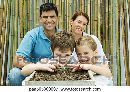 Family together, parents smiling at camera, children touching potted seedling View Large Photo Image Stock Photo - Family together, parents smiling at camera, children touching potted seedling. Fotosearch