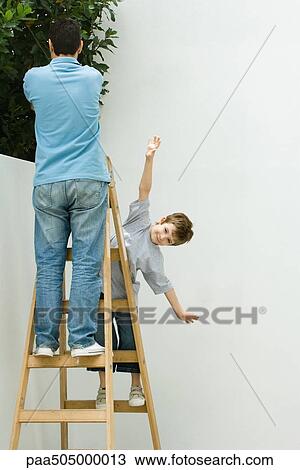 Stock Image - Father and son standing on ladder, boy pretending to be a plane. Fotosearch