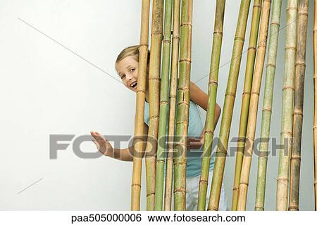 Girl standing behind bamboo, smiling and waving at camera View Large Photo Image Stock Photograph - Girl standing behind bamboo, smiling and waving at camera. Fotosearch