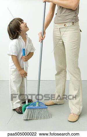 Stock Image - Little boy helping his mother sweep the floor, cropped view. Fotosearch