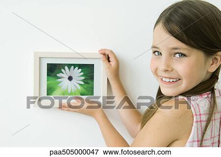 Little girl holding framed picture against wall, smiling over shoulder at camera View Large Photo Image Stock Photo - Little girl holding framed picture against wall, smiling over shoulder at camera. Fotosearch
