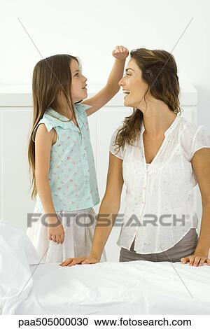 Stock Image - Little girl standing beside kneeling mother, comparing height with her hand. Fotosearch