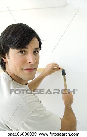 Man nailing thin piece of wood to wall, looking back over shoulder at camera View Large Photo Image Stock Photo - Man nailing thin piece of wood to wall, looking back over shoulder at camera. Fotosearch