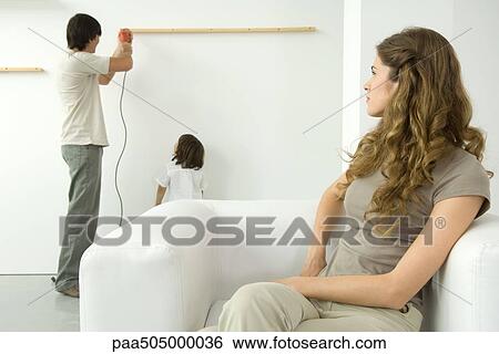 Stock Photograph - Man using drill to attach wood to wall, woman in foreground watching over her shoulder. Fotosearch
