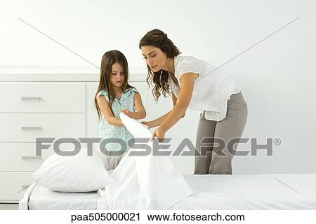 Stock Image - Mother and daughter making bed together. Fotosearch