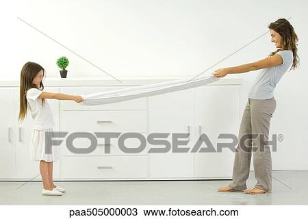 Stock Image - Mother and daughter pulling on opposite ends of sheet. Fotosearch