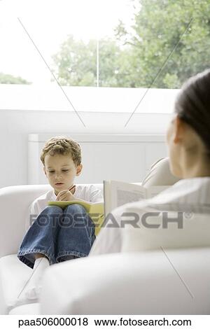 Boy sitting on couch, writing in book, woman reading book in the foreground View Large Photo Image Stock Photo - Boy sitting on couch, writing in book, woman reading book in the foreground. Fotosearch