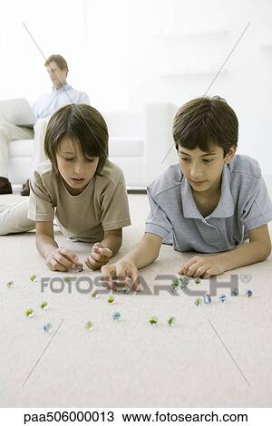 Boys lying on the floor playing with marbles, father sitting on sofa with laptop in background View Large Photo Image Stock Image - Boys lying on the floor playing with marbles, father sitting on sofa with laptop in background. Fotosearch