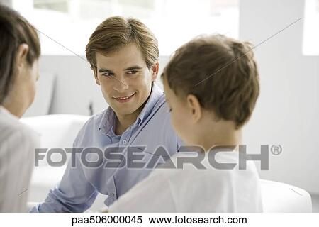 Family sitting together, focus on father smiling at young son View Large Photo Image Stock Photography - Family sitting together, focus on father smiling at young son. Fotosearch