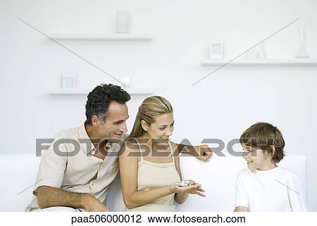 Family sitting together on sofa, mother holding tiny present in her hand View Large Photo Image Stock Image - Family sitting together on sofa, mother holding tiny present in her hand. Fotosearch