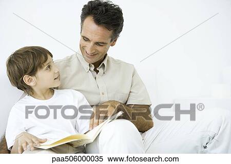 Father and son sitting side by side, smiling at each other, holding book open together View Large Photo Image Stock Photography - Father and son sitting side by side, smiling at each other, holding book open together. Fotosearch