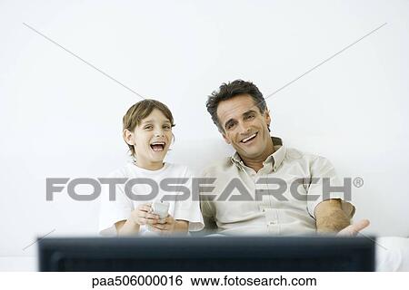 Father and son watching TV together, boy holding remote View Large Photo Image Stock Photograph - Father and son watching TV together, boy holding remote. Fotosearch