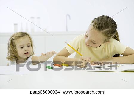 Girl doing homework, younger sister reaching for markers View Large Photo Image Picture - Girl doing homework, younger sister reaching for markers. Fotosearch