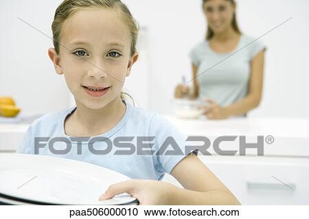 Girl holding plates, smiling at camera, mother in background View Large Photo Image Stock Image - Girl holding plates, smiling at camera, mother in background. Fotosearch