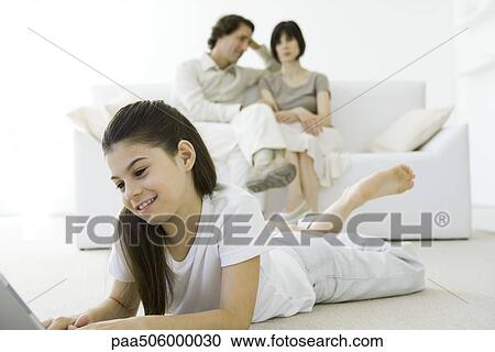 Girl lying on stomach on the floor, parents sitting on couch in background View Large Photo Image Stock Image - Girl lying on stomach on the floor, parents sitting on couch in background. Fotosearch