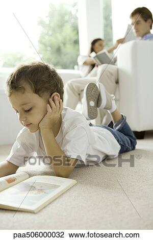 Little boy lying on floor and reading book, parents reading on sofa in background View Large Photo Image Stock Image - Little boy lying on floor and reading book, parents reading on sofa in background. Fotosearch