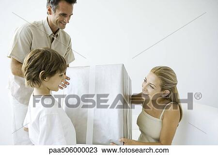 Stock Image - Man giving large gift to woman, son standing nearby and watching. Fotosearch