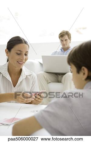 Woman playing a card game with her son, husband sitting in background with laptop View Large Photo Image Stock Photo - Woman playing a card game with her son, husband sitting in background with laptop. Fotosearch