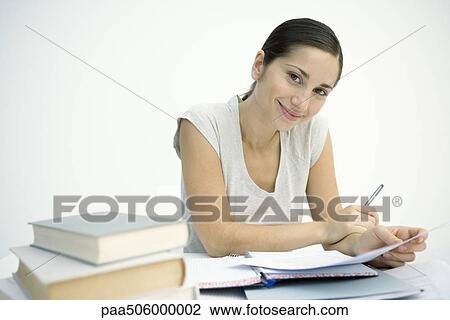 Woman working at table, holding pen and paper, smiling at camera View Large Photo Image Stock Image - Woman working at table, holding pen and paper, smiling at camera. Fotosearch