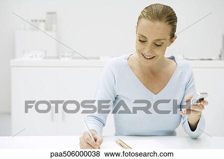 Woman writing in notebook and holding cell phone View Large Photo Image Stock Photo - Woman writing in notebook and holding cell phone. Fotosearch