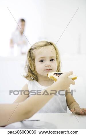 Young girl sitting at table, being fed a piece of bread with jam, cropped view View Large Photo Image Stock Photograph - Young girl sitting at table, being fed a piece of bread with jam, cropped view. Fotosearch