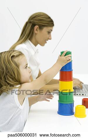Young girl stacking multi-colored cylinders, young woman using laptop in background View Large Photo Image Stock Image - Young girl stacking multi-colored cylinders, young woman using laptop in background. Fotosearch