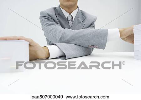 Stock Photo - Man crossing his arms to put hands on top of stacks of paper, cropped view. Fotosearch