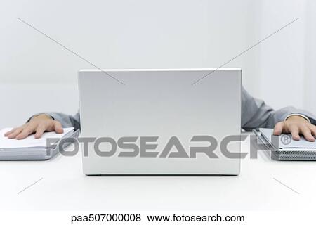 Stock Photo - Man hiding laptop putting palms on stacks of paper to either side. Fotosearch